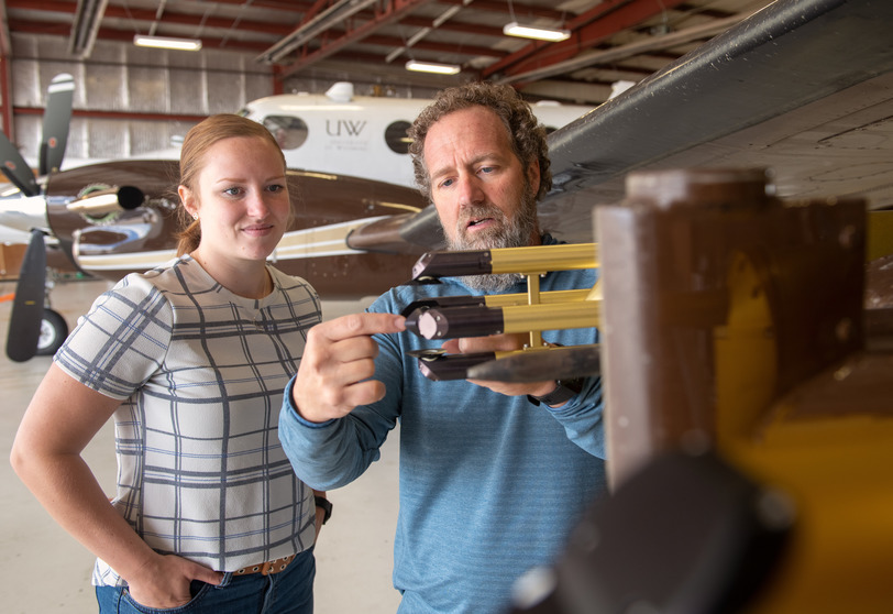 Two people look at a diagnostic insturment in an airplane hanger