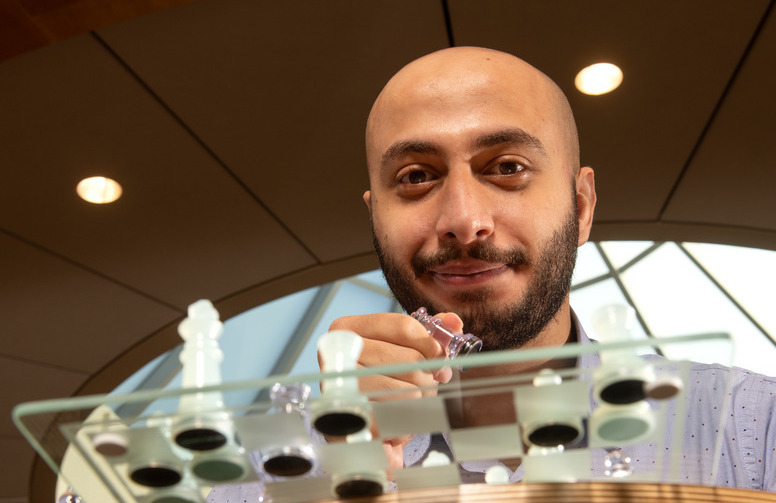 A student smiles for the camera while playing chess