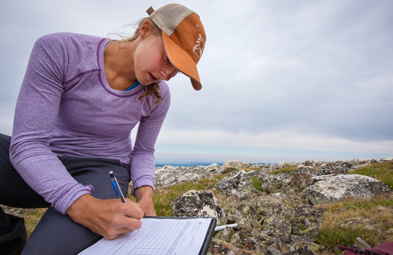 A student writes on a piece of paper while out in the field during class