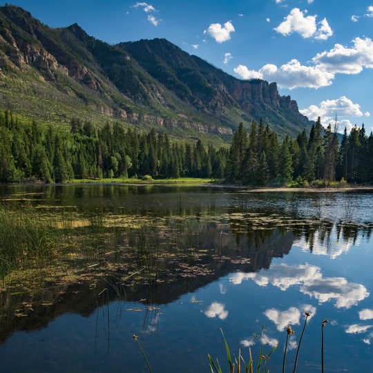 a blue sky is reflected in a lake next to mountains and trees