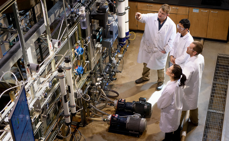 Professor and students in lab coats looking at hydrology lab equipment