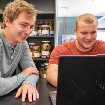 Two students look at a laptop in a lab