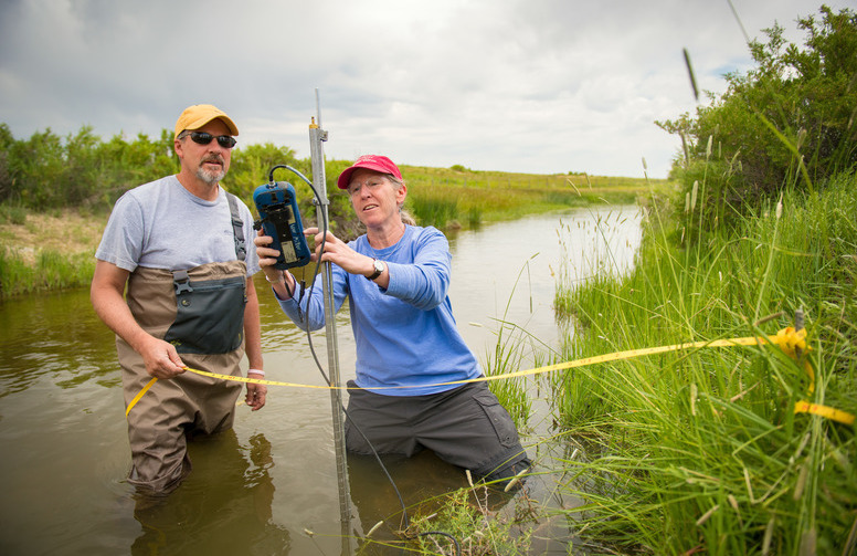 Two researchers standing in a river taking stats on the water
