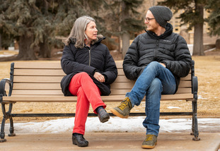 Two people talking on a bench. 