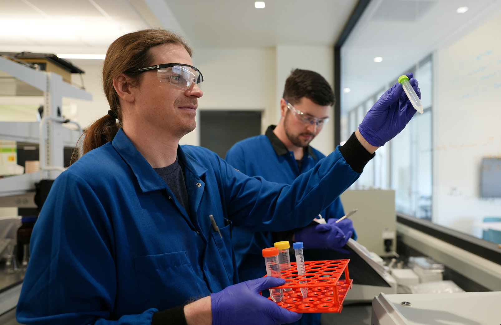 Two graduate students in lab coats reach for materials in a lab