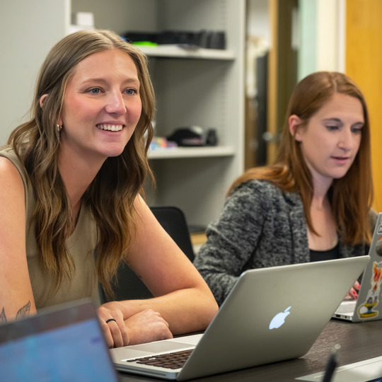 Two female students participate in a class with laptops open.