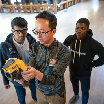 Three people use equipment to do engineering research in a building.