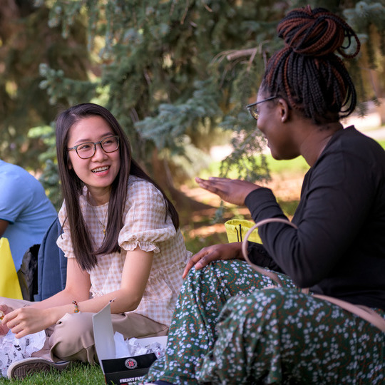 Two students sit outside and have a conversation.