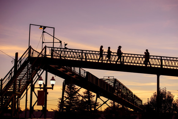 Silhouetted pedestrian bridge at sunset with people walking on it against a colorful sky.