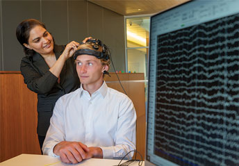 professor fits a headpiece on a student to measure brain waves