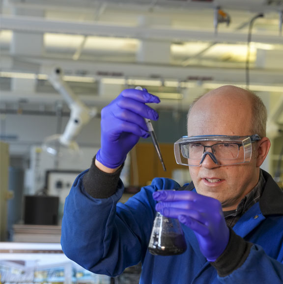 man wearing safety goggles and gloves holding a beaker