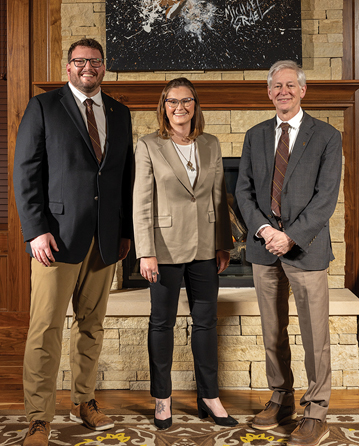 three people pose by a fireplace