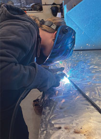 student in a helmet works on a welding art project