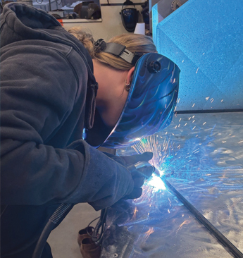 student in a helmet works on a welding art project