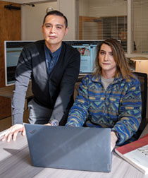 Staff member and a student working on a laptop next to a patent book
