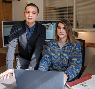 Staff member and a student working on a laptop next to a patent book