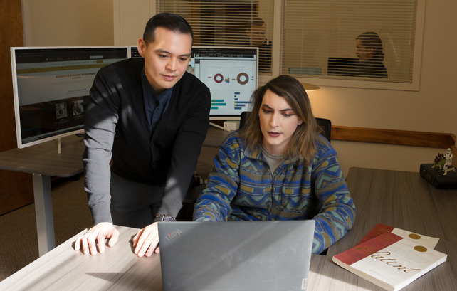 Staff member and a student working on a laptop next two patent books