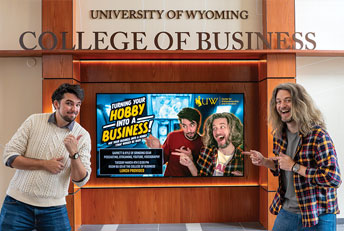 Two man pointing at a screen advertising their speech in the UW College of Business