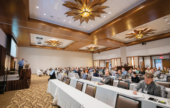 large ballroom space with people at tables listening to a presenter