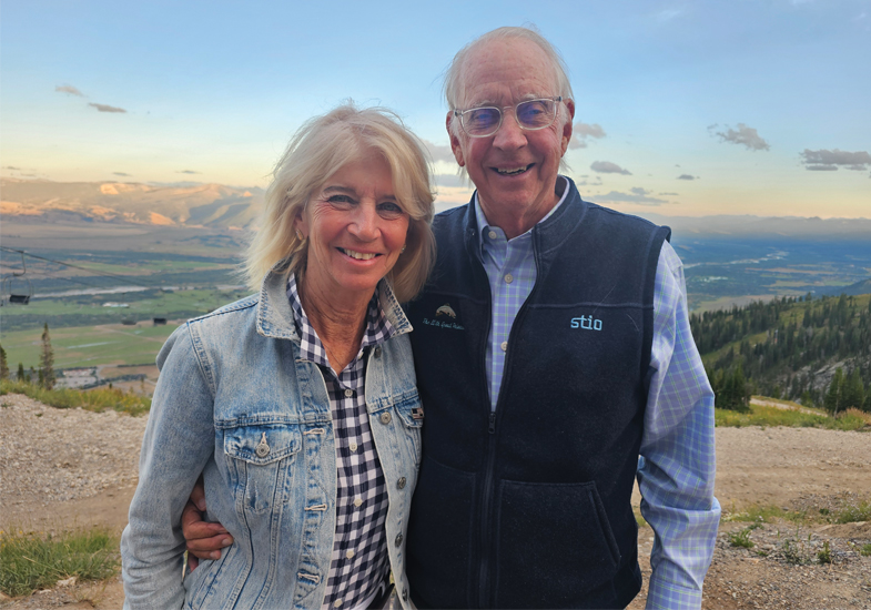 A couple smiles while standing together on a mountain overlook at sunset