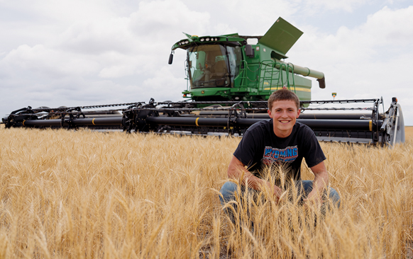 man sitting in a wheat field in front of a large tractor