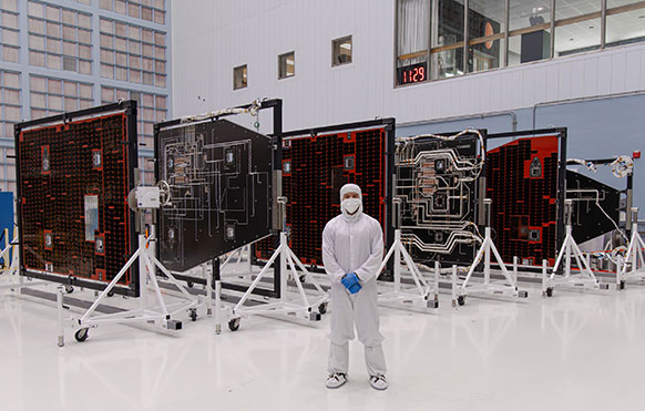 man in a full body suit in a large room of sun shields for a telescope