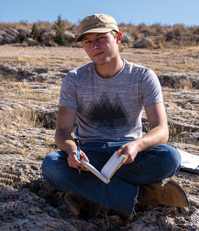 Male student with an open notebook sitting on the ground on Pilot Hill