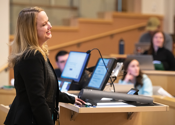 female professor at a podium lectures students