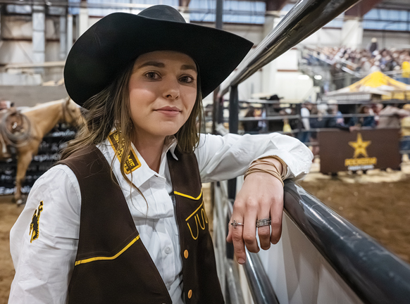 student in a white shirt, brown vest, and brown cowboy hat at a rodeo