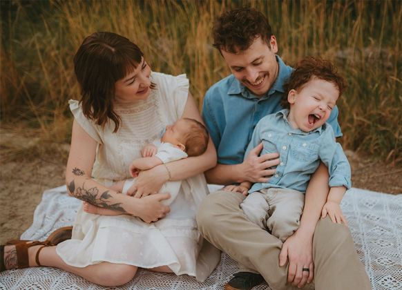 Family with young children sit on a blanket in a field