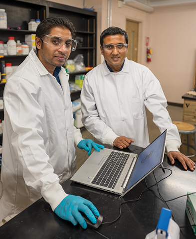 Two researchers in lab coats in a lab with a computer