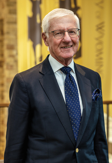 Man in dark blue suit with blue tie with UW flags behind him