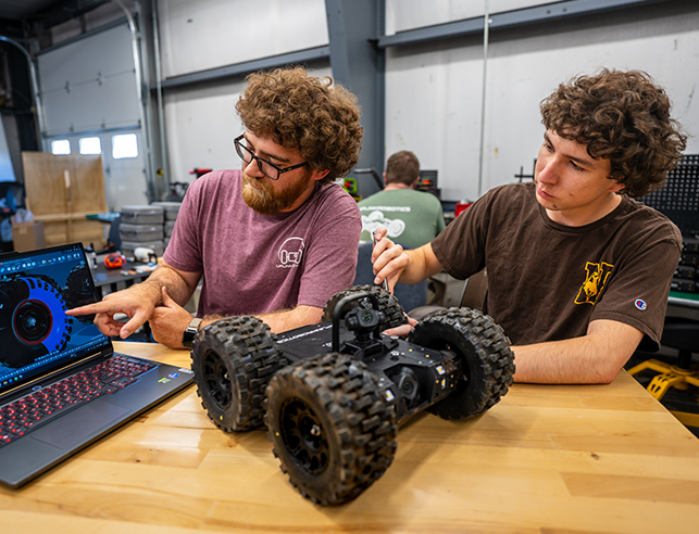 Two people working on a laptop and a robot