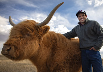 man with an arm over a shaggy cow with long horns