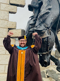 man in cap and gown in front of bucking horse statue
