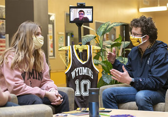 a woman and a man sitting down, wearing masks and talking