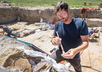 man brushing dirt away from a fossil at a dig