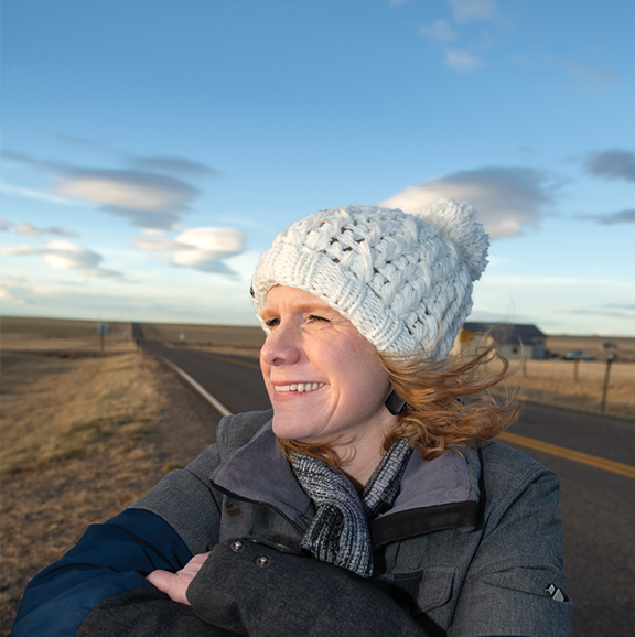 person in a beanie with a pom-pom on it standing in front of an open highway