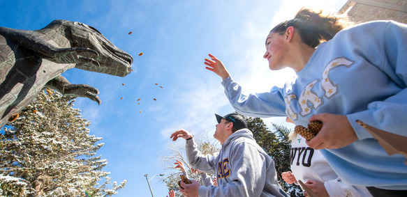 Students throwing pinecones into Rexy's mouth