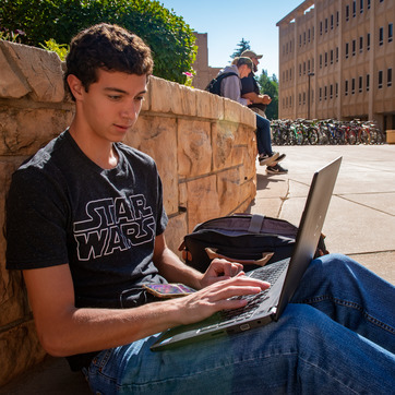 Student with laptop sitting outside of the Classroom Building