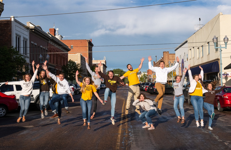 A group of students pose and jump in the air in the middle of a street in downtown Laramie