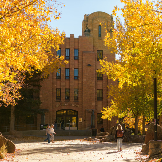 An exterior view of the Wyoming Union building during a sunny fall day with yellow leaves on the trees.