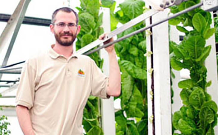 Picture of someone in a green house next to plants growing