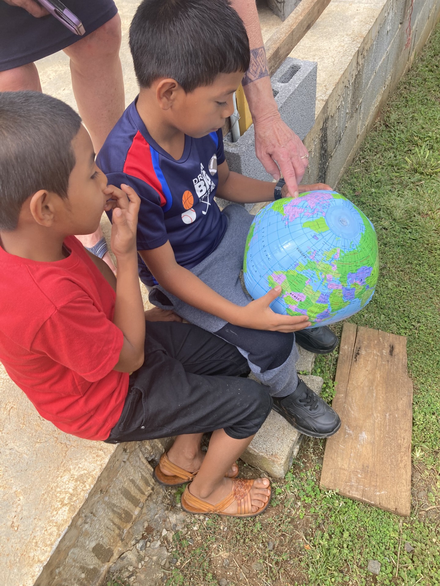 A group of children sitting on a ledge and looking at a inflatable globe.