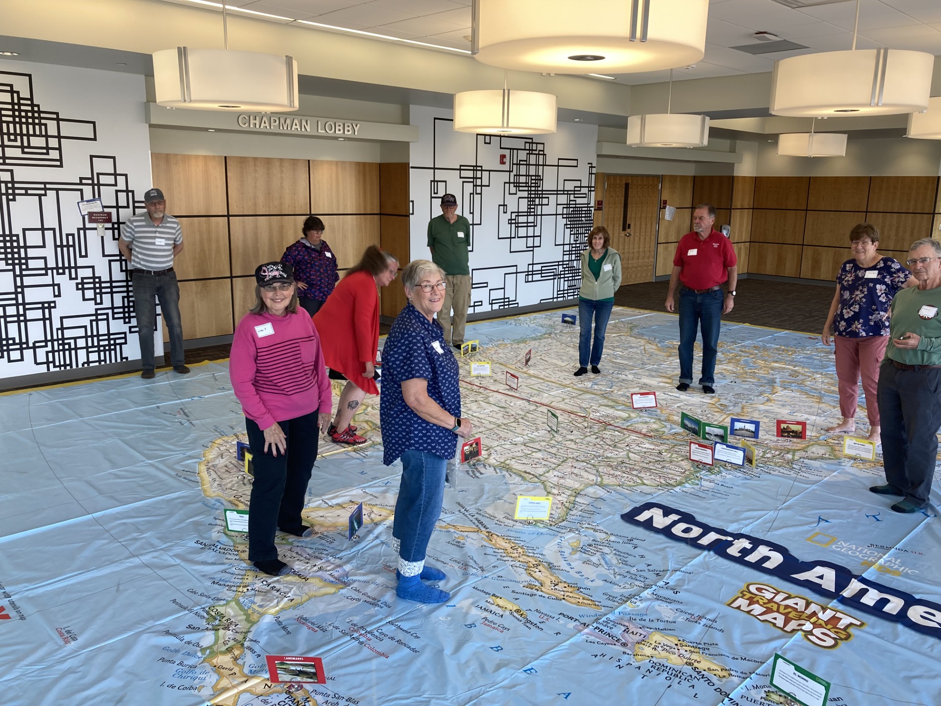 A group of older people standing on a giant floor map and looking down at it.