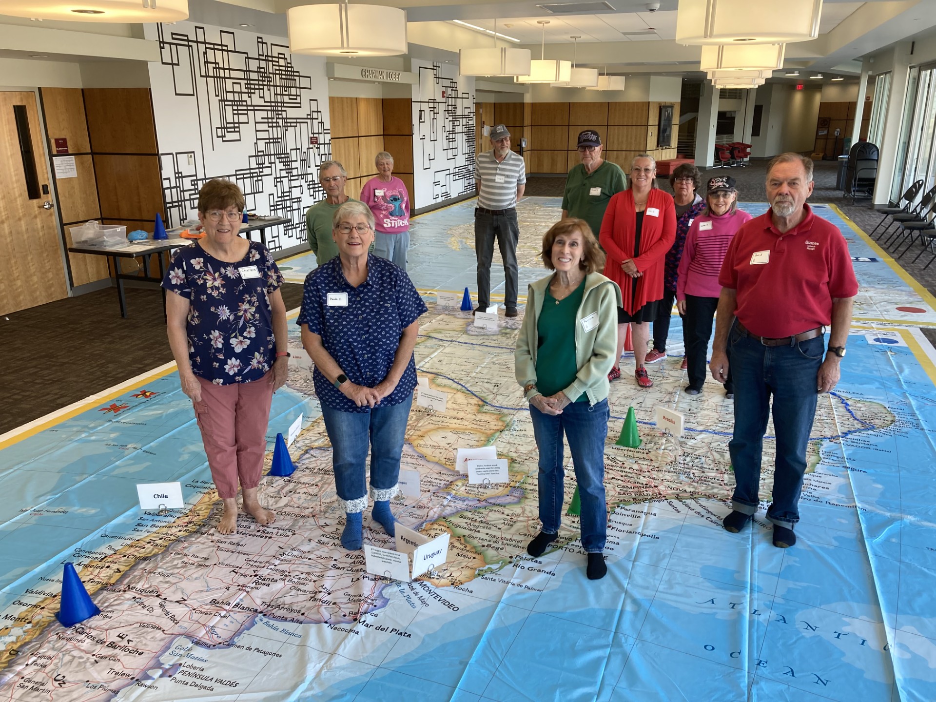 A group of older people standing on a giant floor map and looking at the camera.