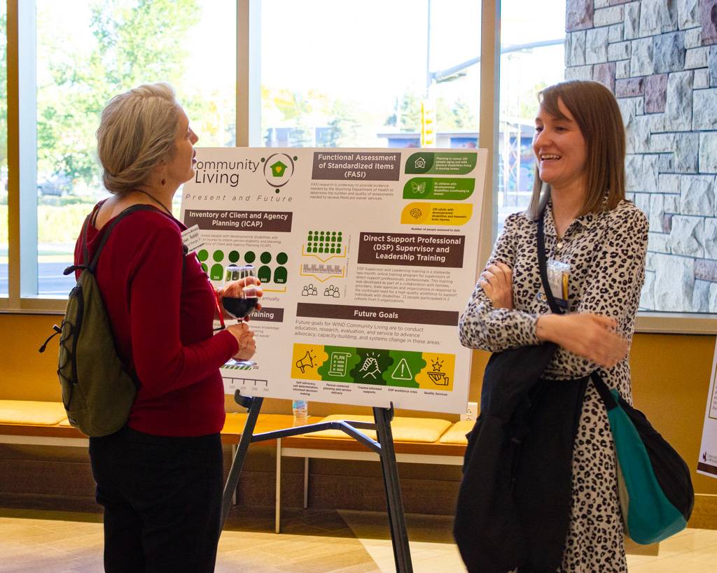 Two people conversing in front of the Community Living poster.