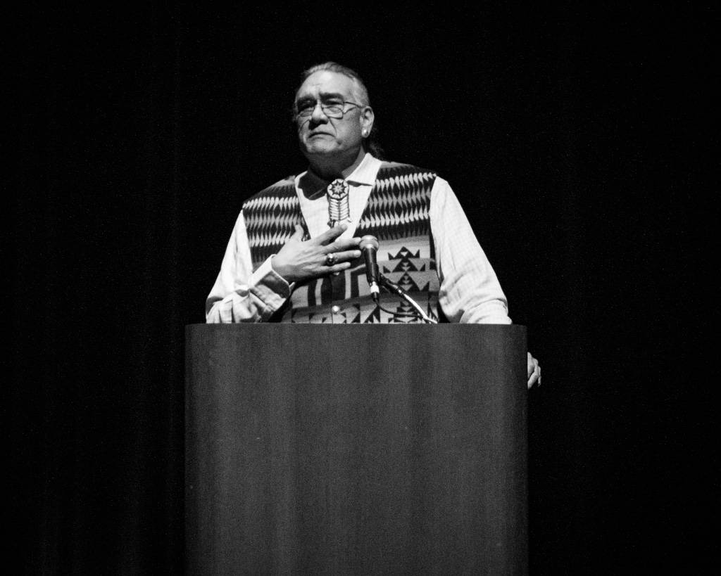 Jim Warne standing behind a podium with a microphone addressing the audience.