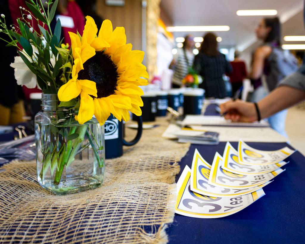 An attendee filling out a sign-up sheet on the WIND registration table decorated with sunflowers and 30th anniversary stickers.