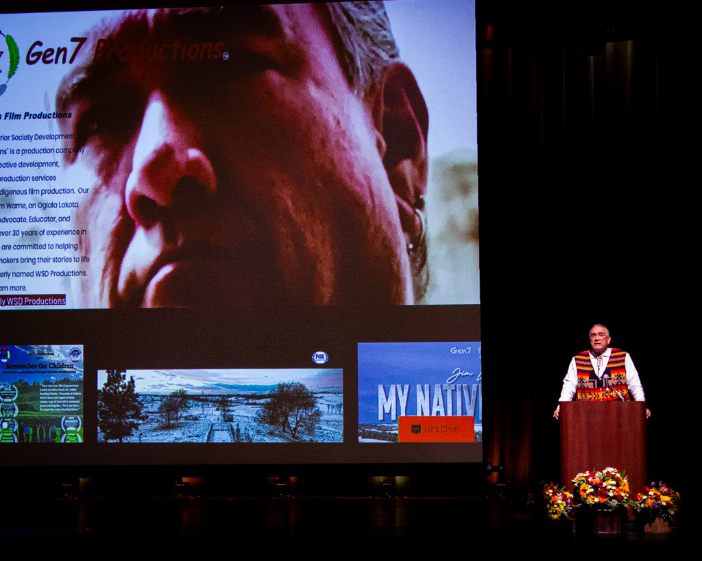 Jim Warne standing behind a podium with a large movie screen in the background